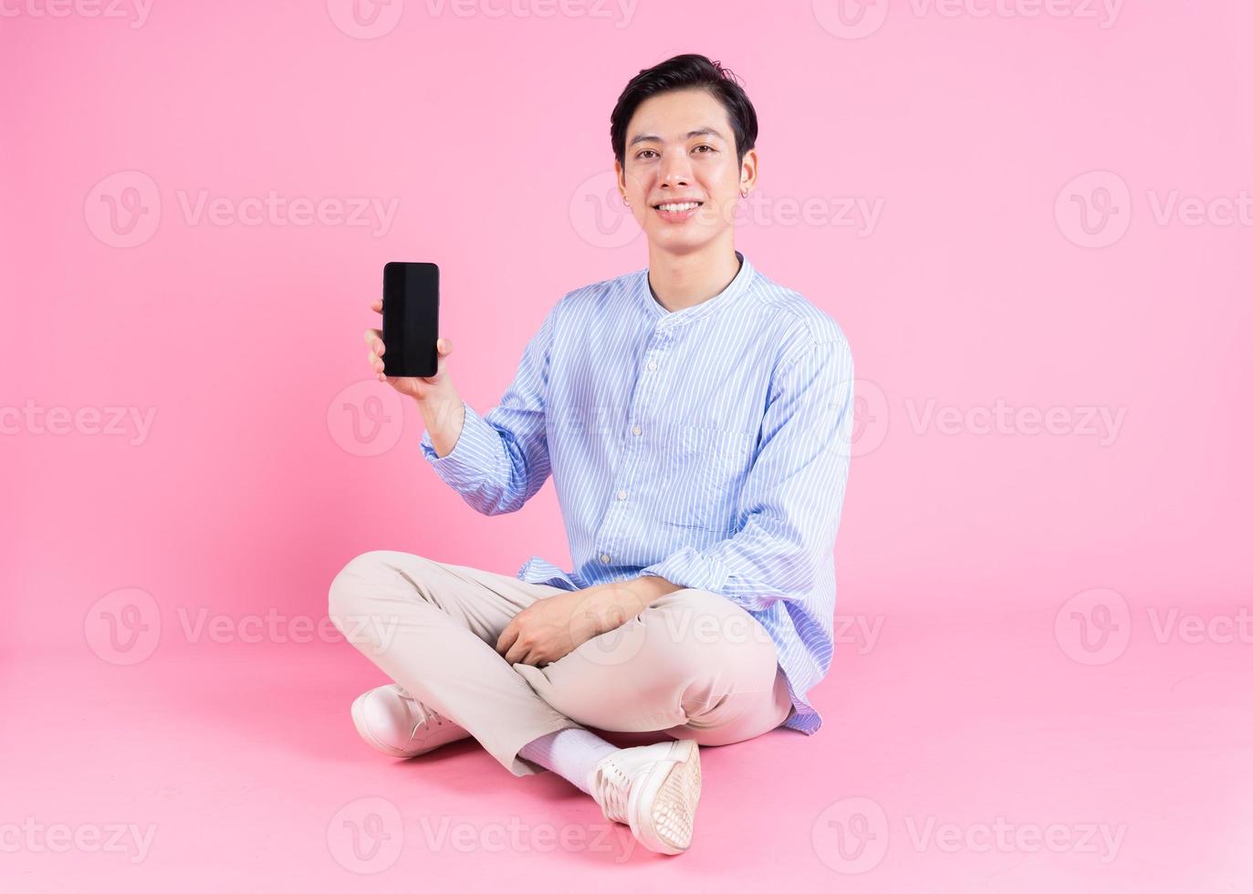 ung asiatisk man Sammanträde och använder sig av smartphone på bakgrund foto