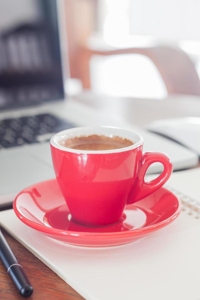 närbild av en kaffekopp med ett anteckningsblock och en bärbar dator foto