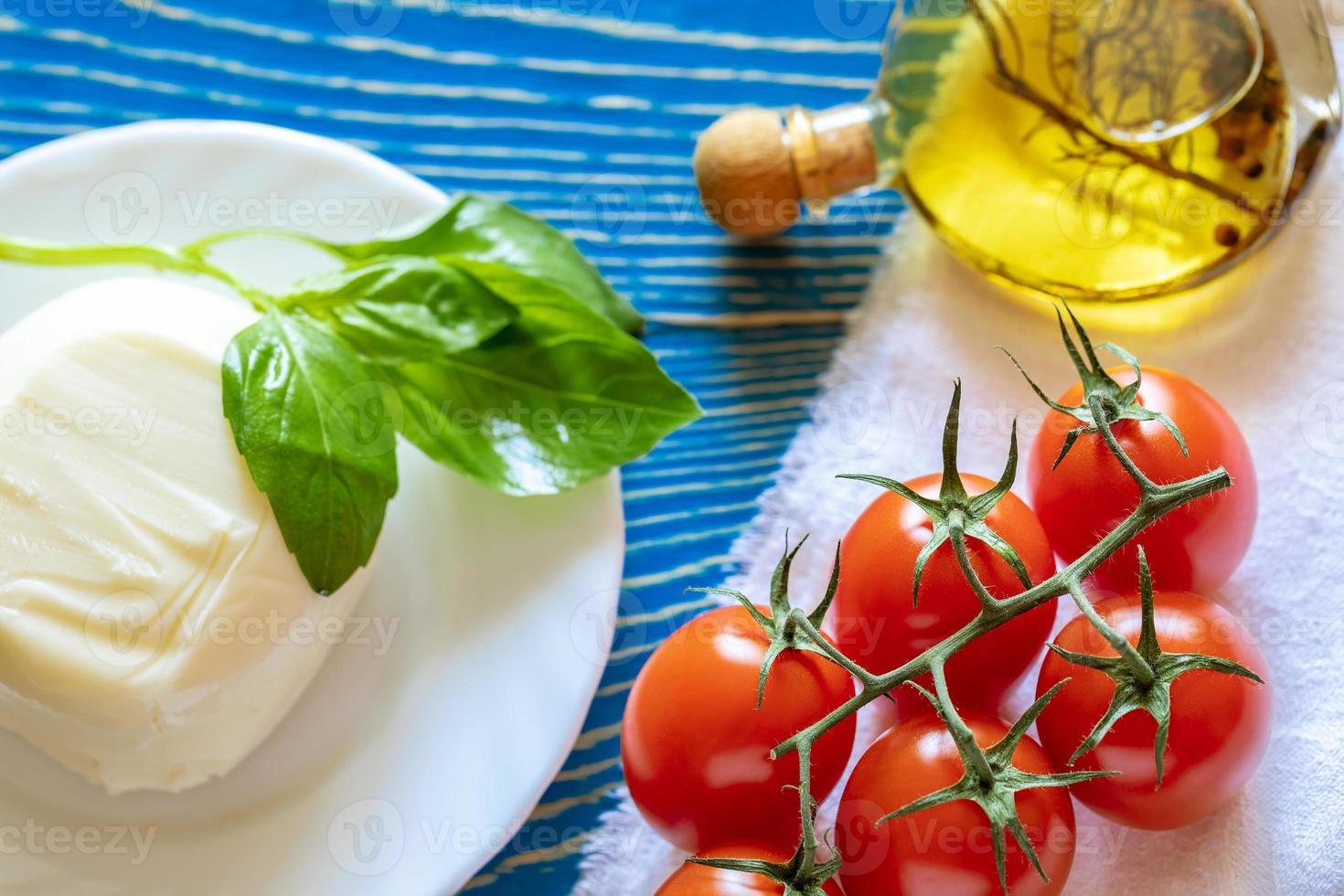 röd tomater, mozzarella ost, oliv olja och basilika på vit kök servett på blå trä- tabell. foto