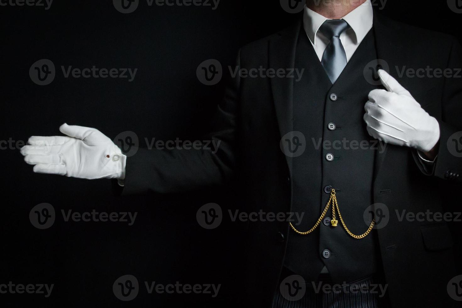 porträtt av butler i mörk kostym och vit handskar stående med välkomnande gest. begrepp av service industri och professionell gästfrihet foto