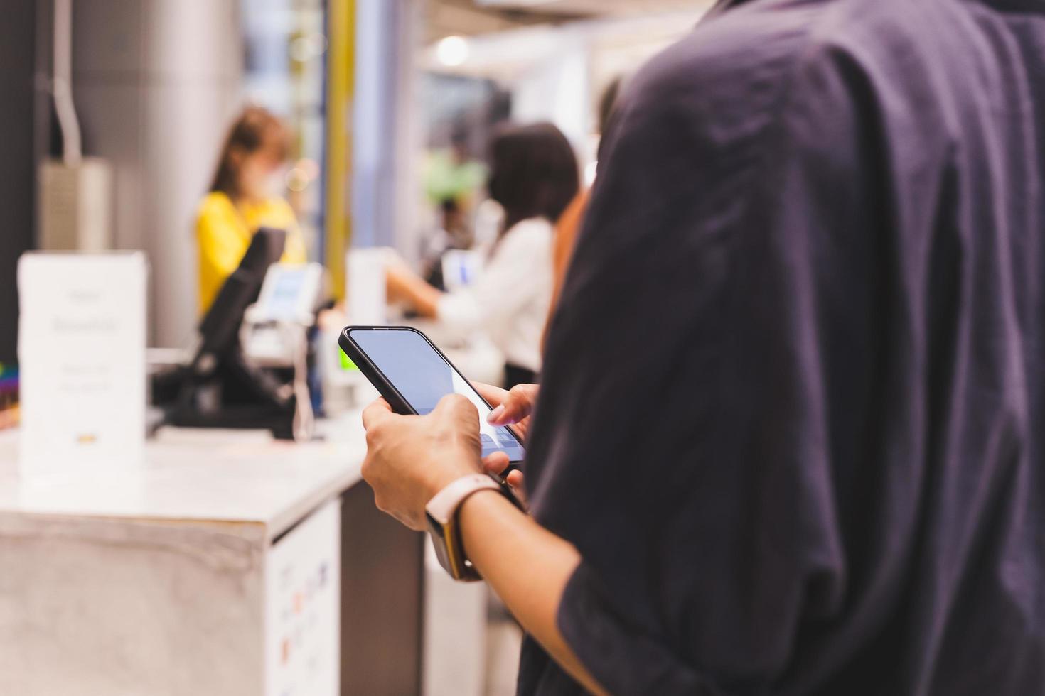 kvinnor använder sig av smart telefon medan väntar för kolla upp ut på cahsier disken. foto