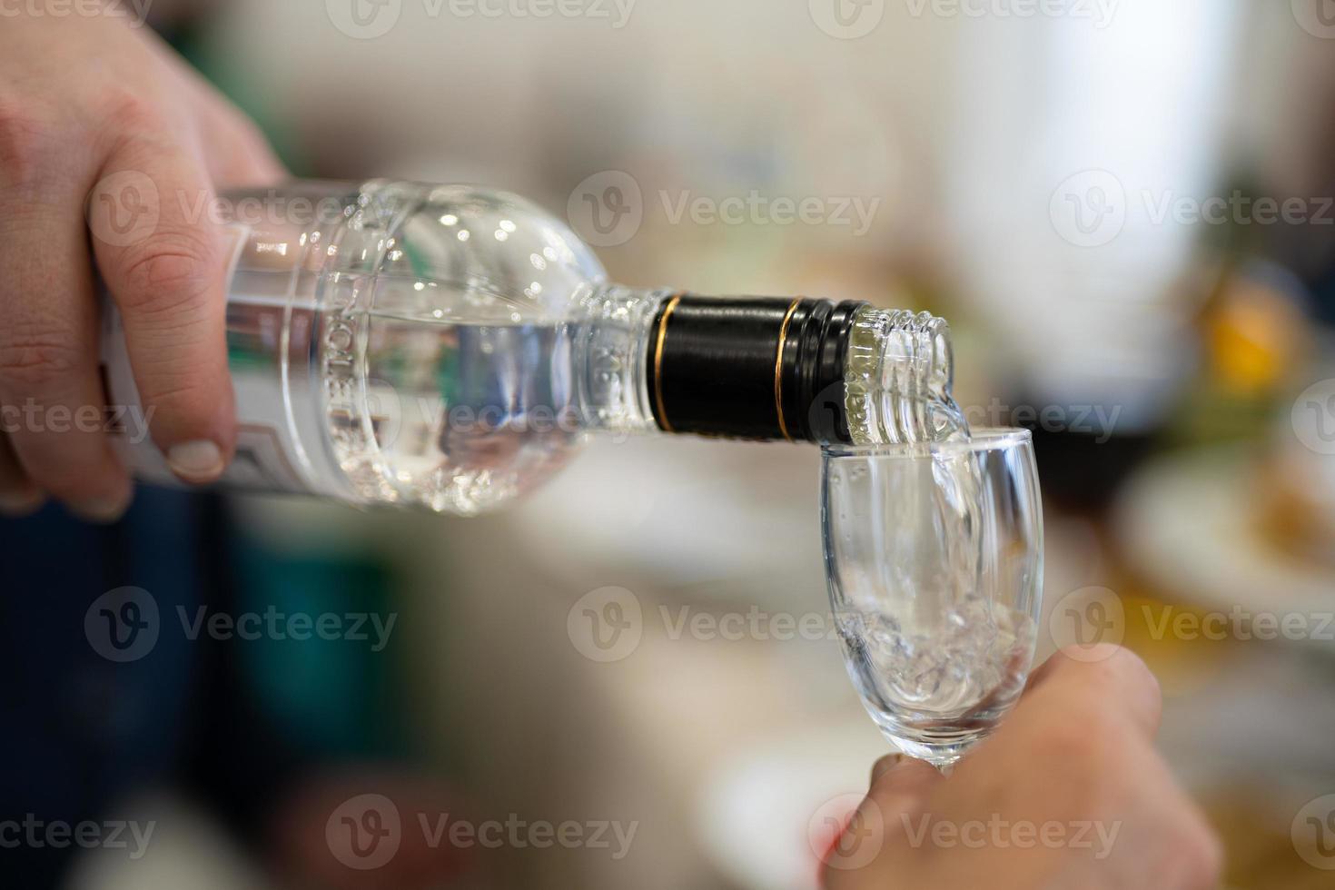 de servitör häller ett alkoholhaltig dryck, vodka in i en glas. foto