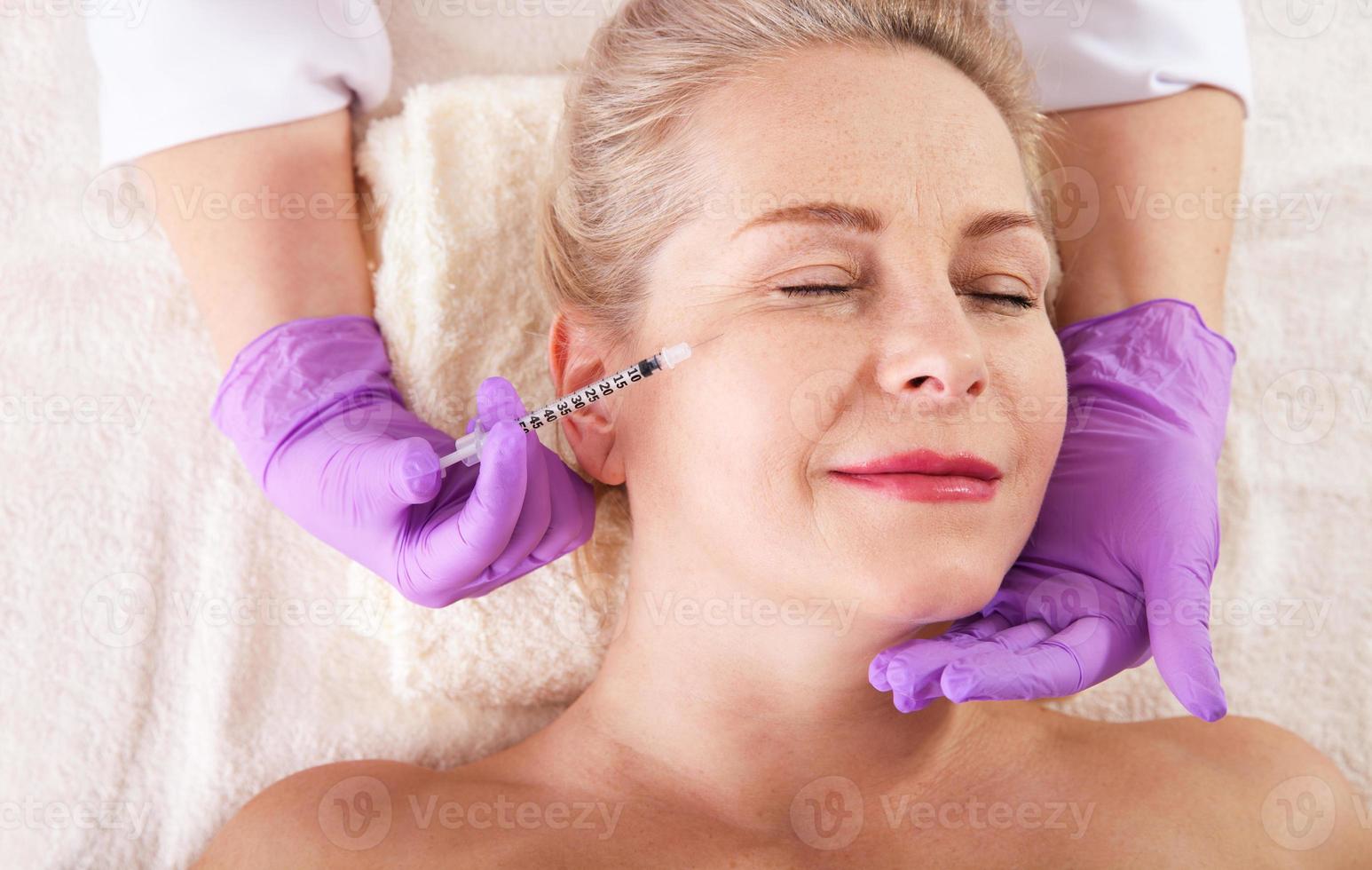 mitten åldrig kvinna får kosmetisk injektion i de ansikte. hyaluronisk syra injektion för ansiktsbehandling föryngring procedur. kvinna i skönhet salong. plast kirurgi klinik. foto