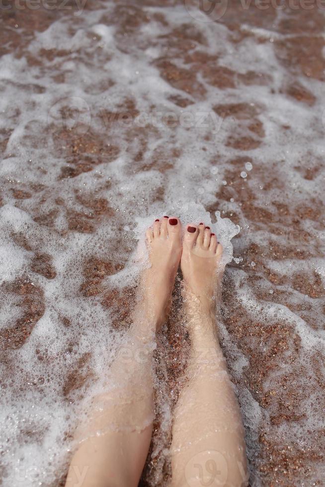 resekoncept - kvinnas ben på vacker tropisk strand med stensand. fötter på sand och våg på sommaren. flicka barfota i havsvatten på semesterresor. känna sig glad och slappna av. kopieringsutrymme. foto