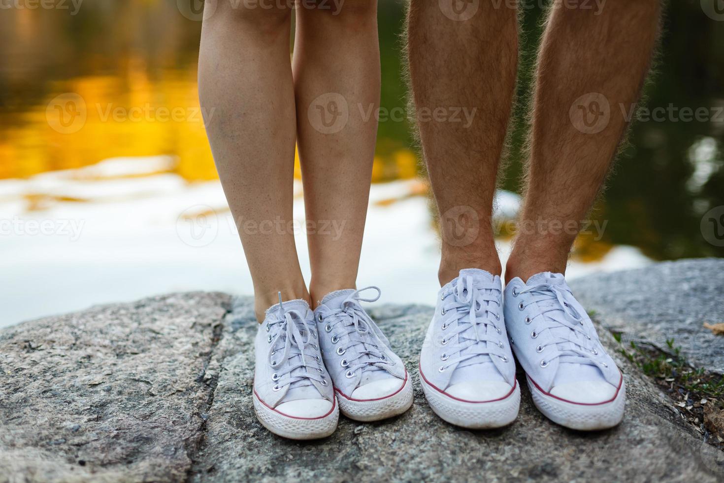 kärlek berättelse berättade förbi stövlar. mänsklig fötter stänga upp. man och kvinna i sneakers. flicka i vit skor. kille i svart gymnastikskor och denim. hipster par i sommar. ben stänga upp. foto