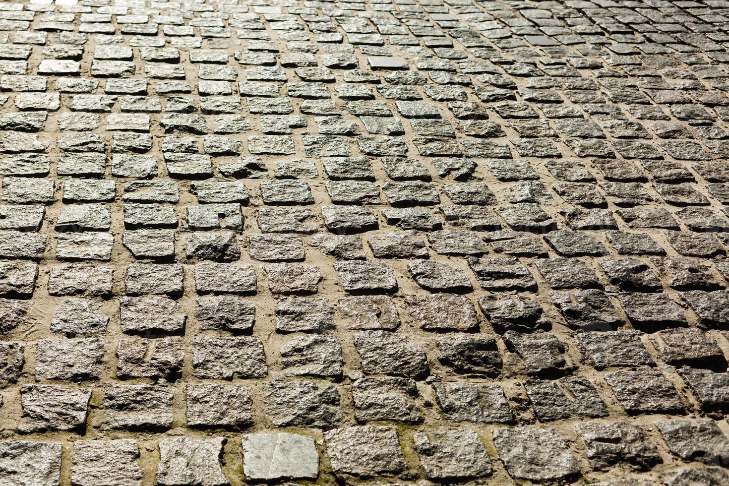 svart kullerstensbelagda sten väg bakgrund med reflexion av ljus sett på de väg. svart eller mörk grå sten trottoar textur. gammal stenläggning sten bakgrund foto