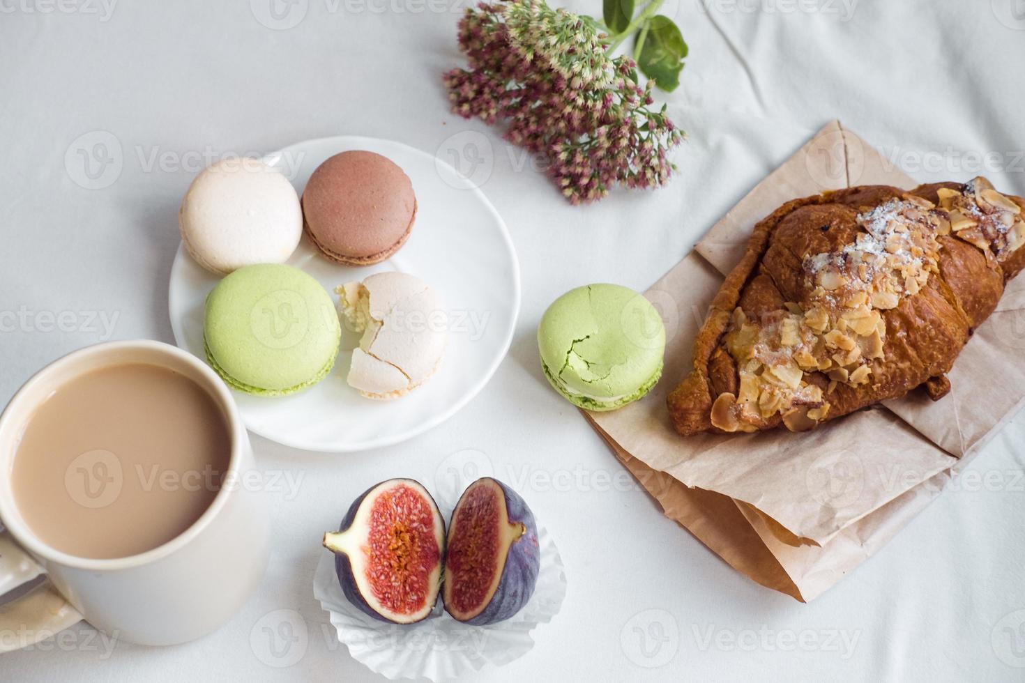 estetik av en kopp av kaffe, fikon, en stor croissant och macarons på en vit bakgrund, topp se foto