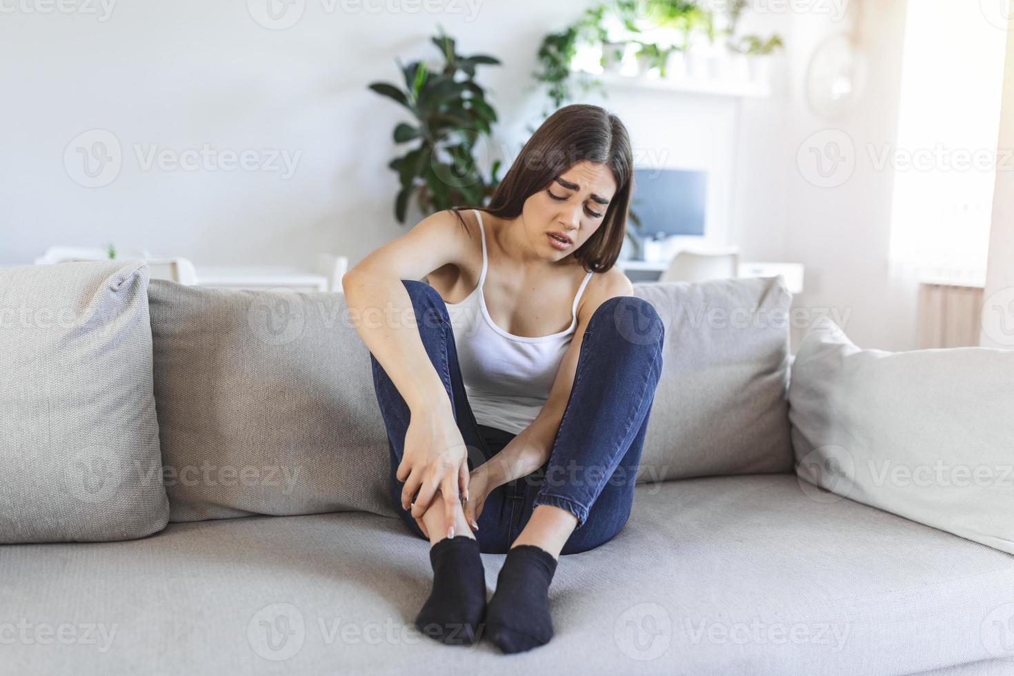 händer masse svullen fot medan Sammanträde på soffa under de dag på Hem. Foto av ung caucasian kvinna lidande från smärta i ben. kvinna masse henne ben efter Allt dag på arbete i kontor