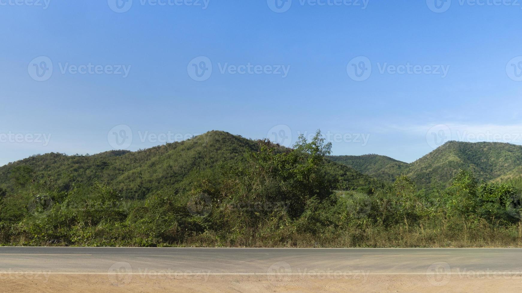 horisontell se av asfalt väg i thailand. bakgrund av grön skog och berg under de blå himmel. foto