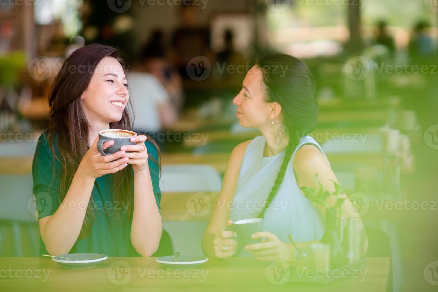 Lycklig leende ung kvinnor med kaffe koppar på Kafé. kommunikation och vänskap begrepp foto