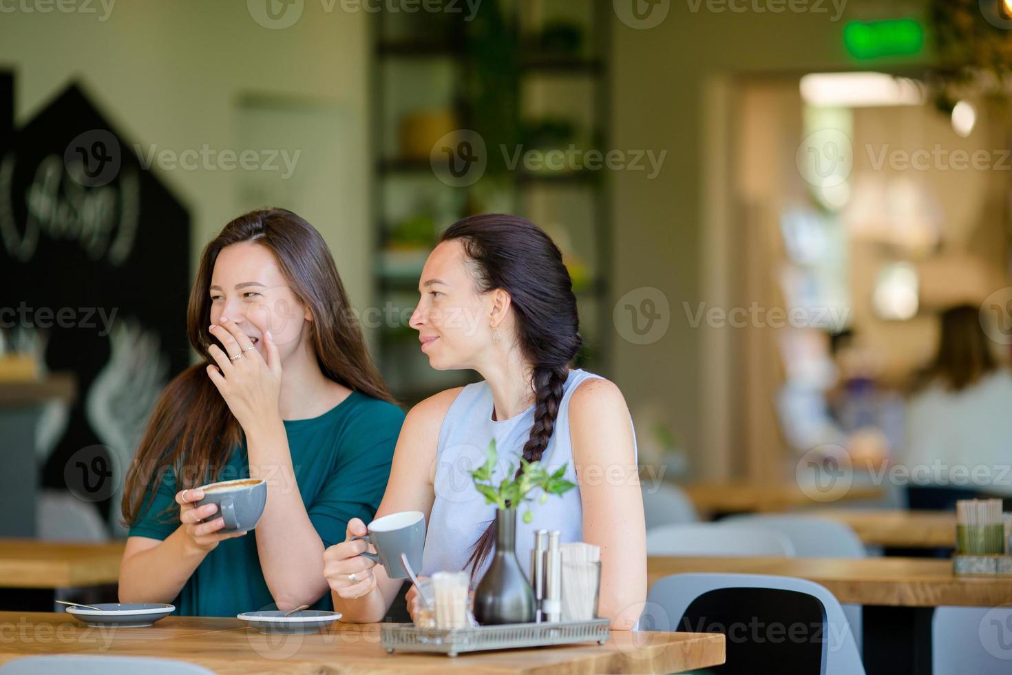 Lycklig leende ung kvinnor med kaffe koppar på Kafé. kommunikation och vänskap begrepp foto