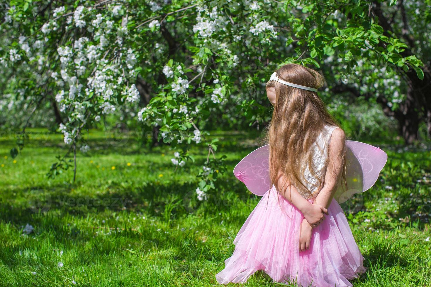 liten söt flicka med fjäril vingar i blomstrande äpple fruktträdgård foto