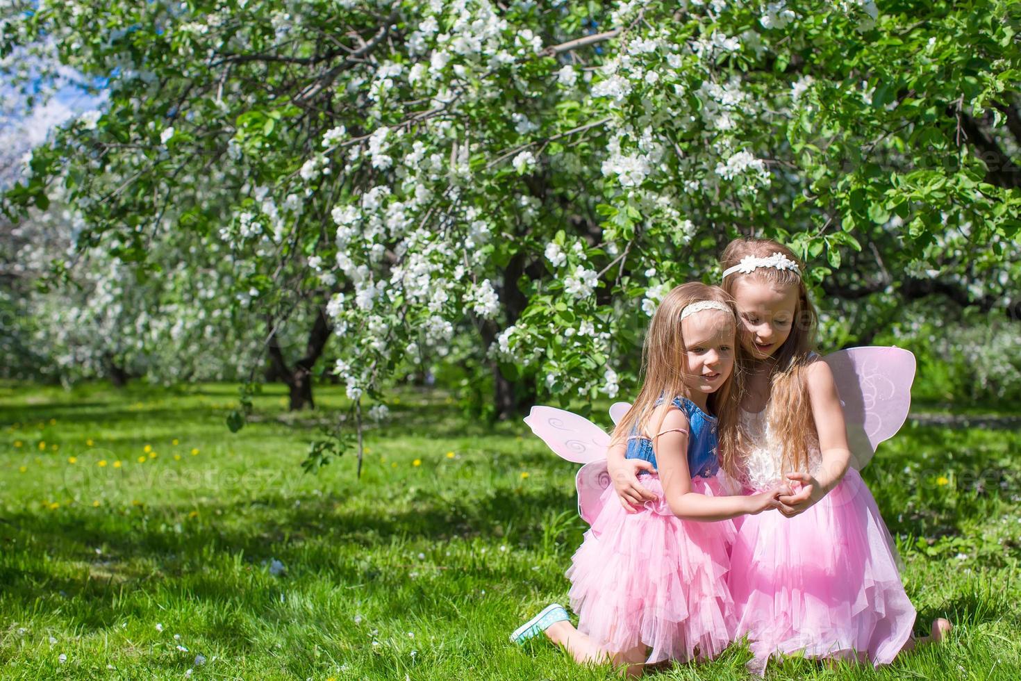 liten förtjusande flickor med fjäril vingar under blomstrande äpple träd foto