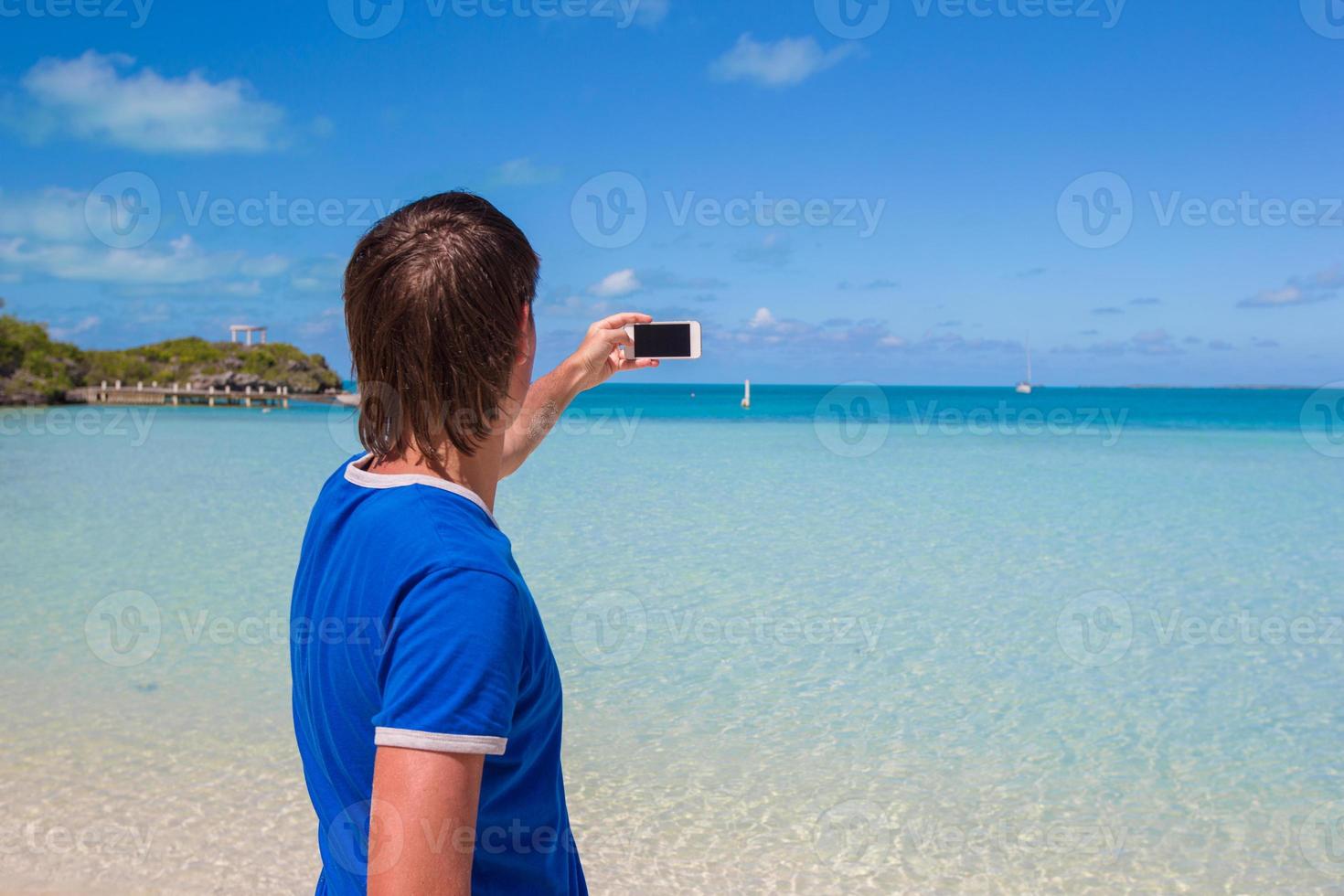 ung man i santa hatt med telefon på tropisk karibiska strand foto