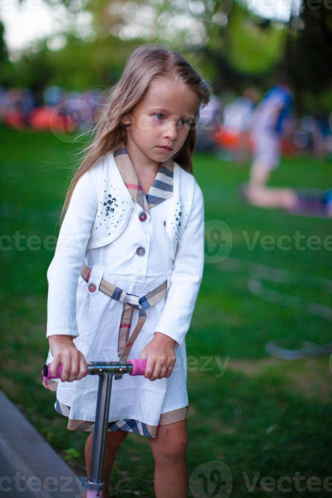 skön litet barn flicka på de skoter i en parkera foto