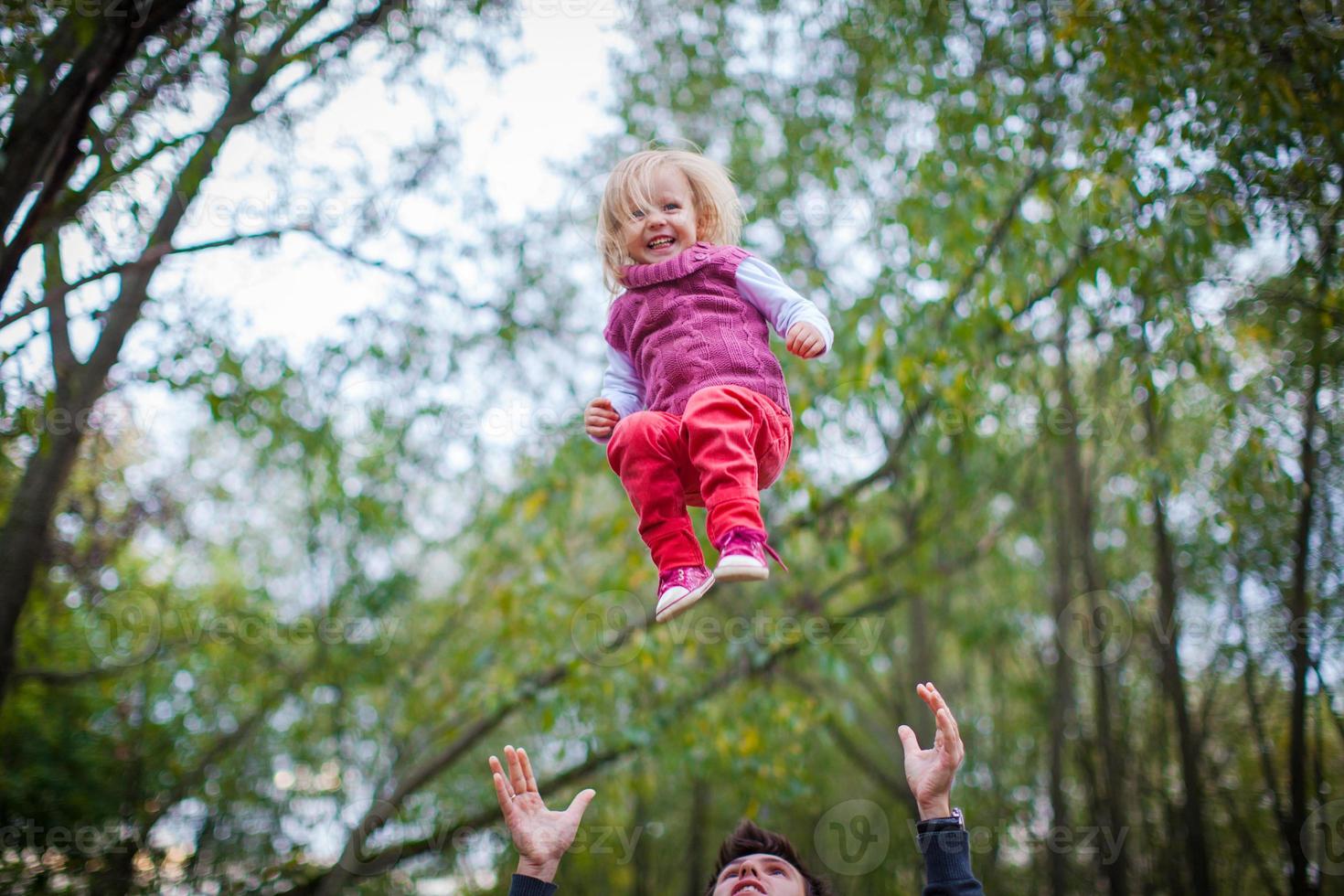 friska far kastar hans liten smilande dotter i de parkera foto