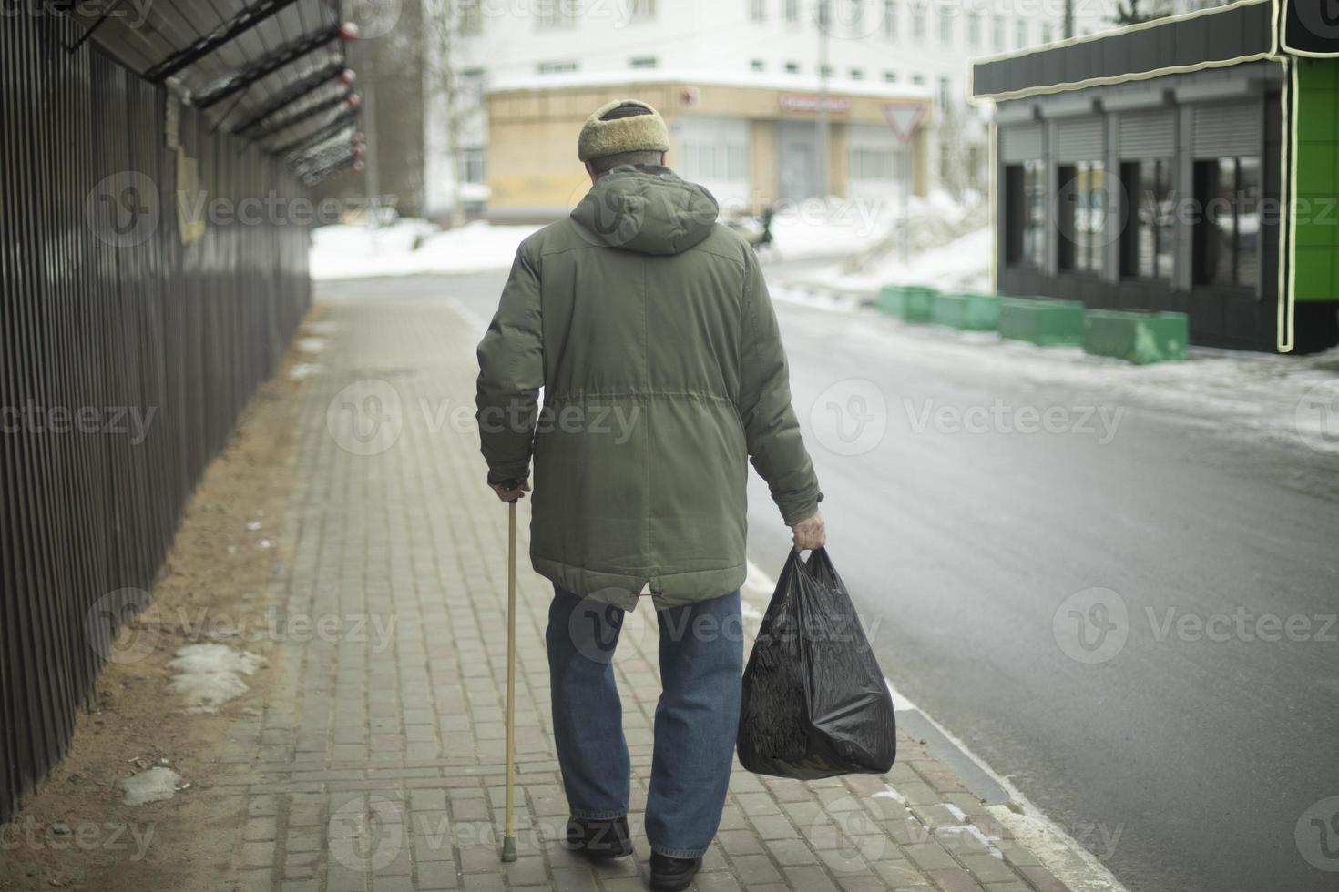 pensionär promenader med väska i hans hand. man med gående pinne. foto