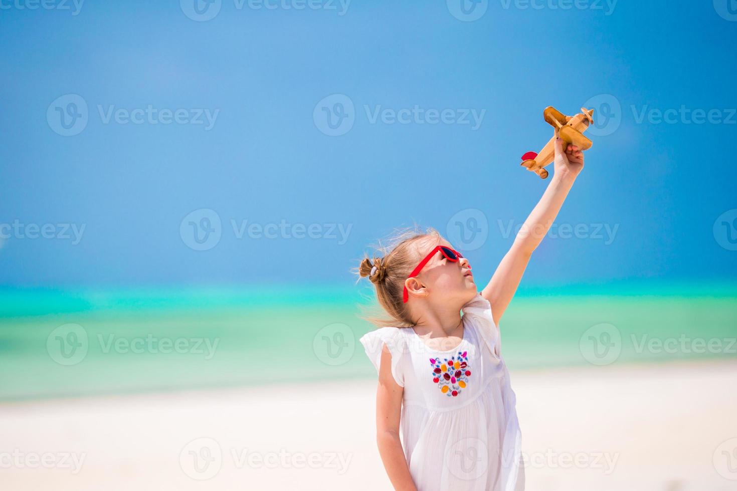 bedårande liten flicka med leksaksflygplan i händerna på den vita tropiska stranden foto