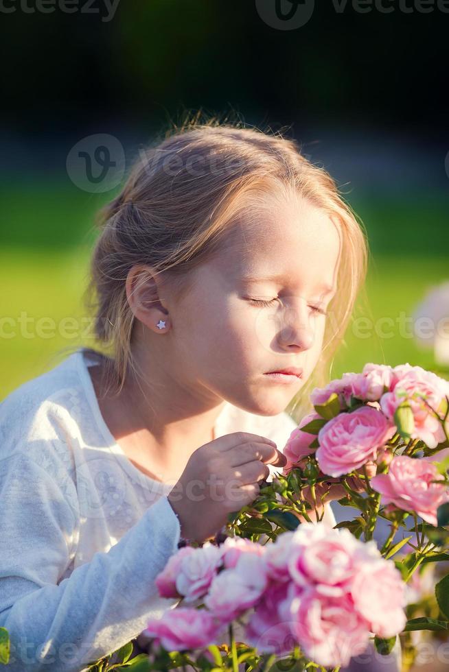liten förtjusande flicka lukta färgrik blommor utomhus foto