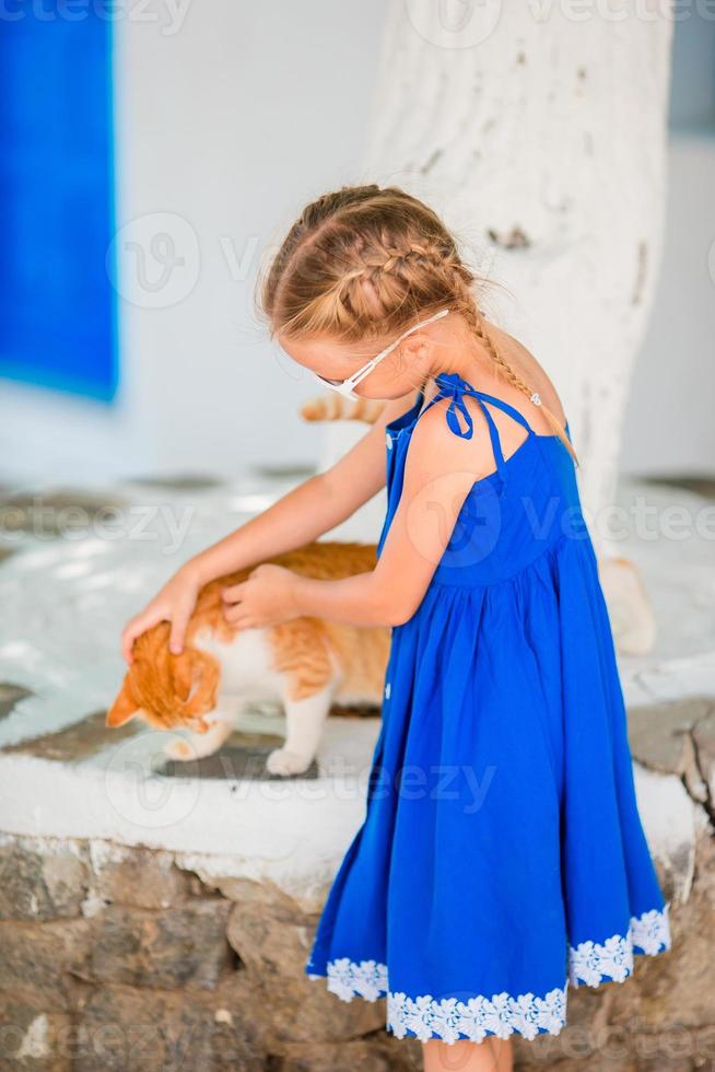 liten förtjusande flicka spelar med ingefära katt i grekisk by utomhus- foto