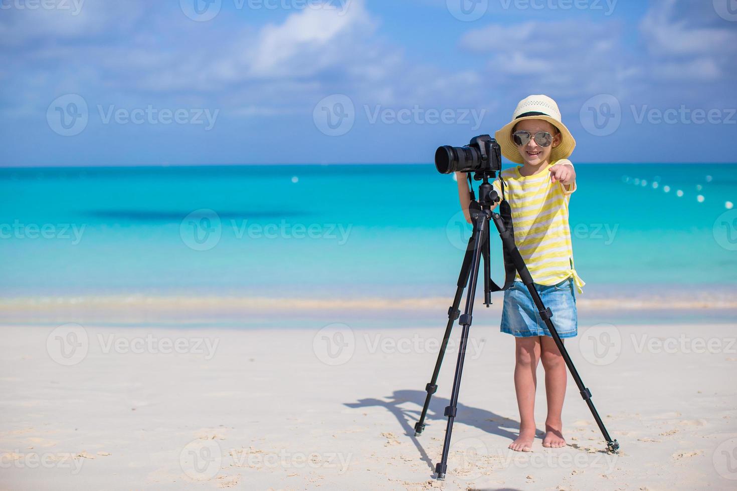 liten flicka skytte med kamera på stativ under henne sommar semester foto