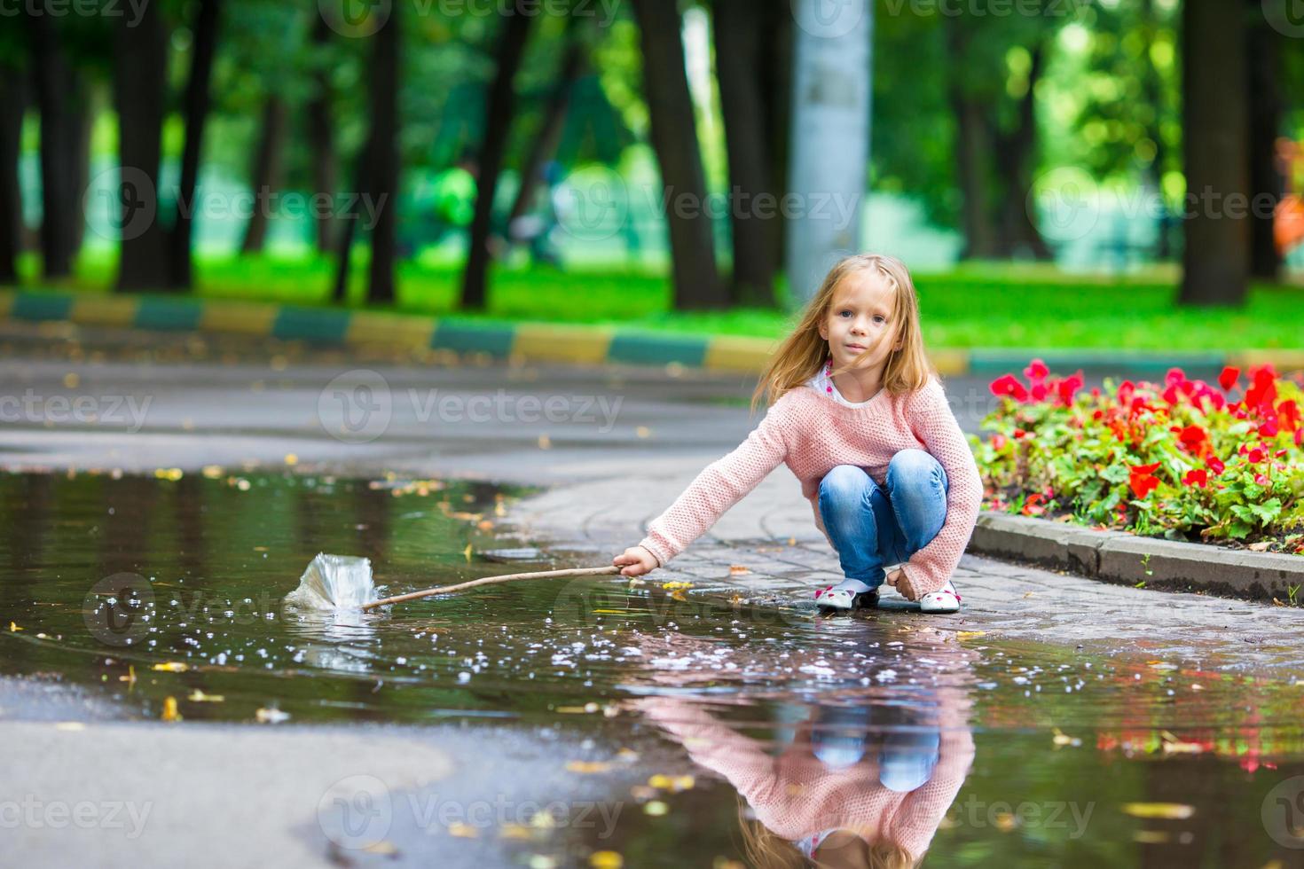 liten Lycklig flicka har roligt i en stor pöl i höst parkera foto