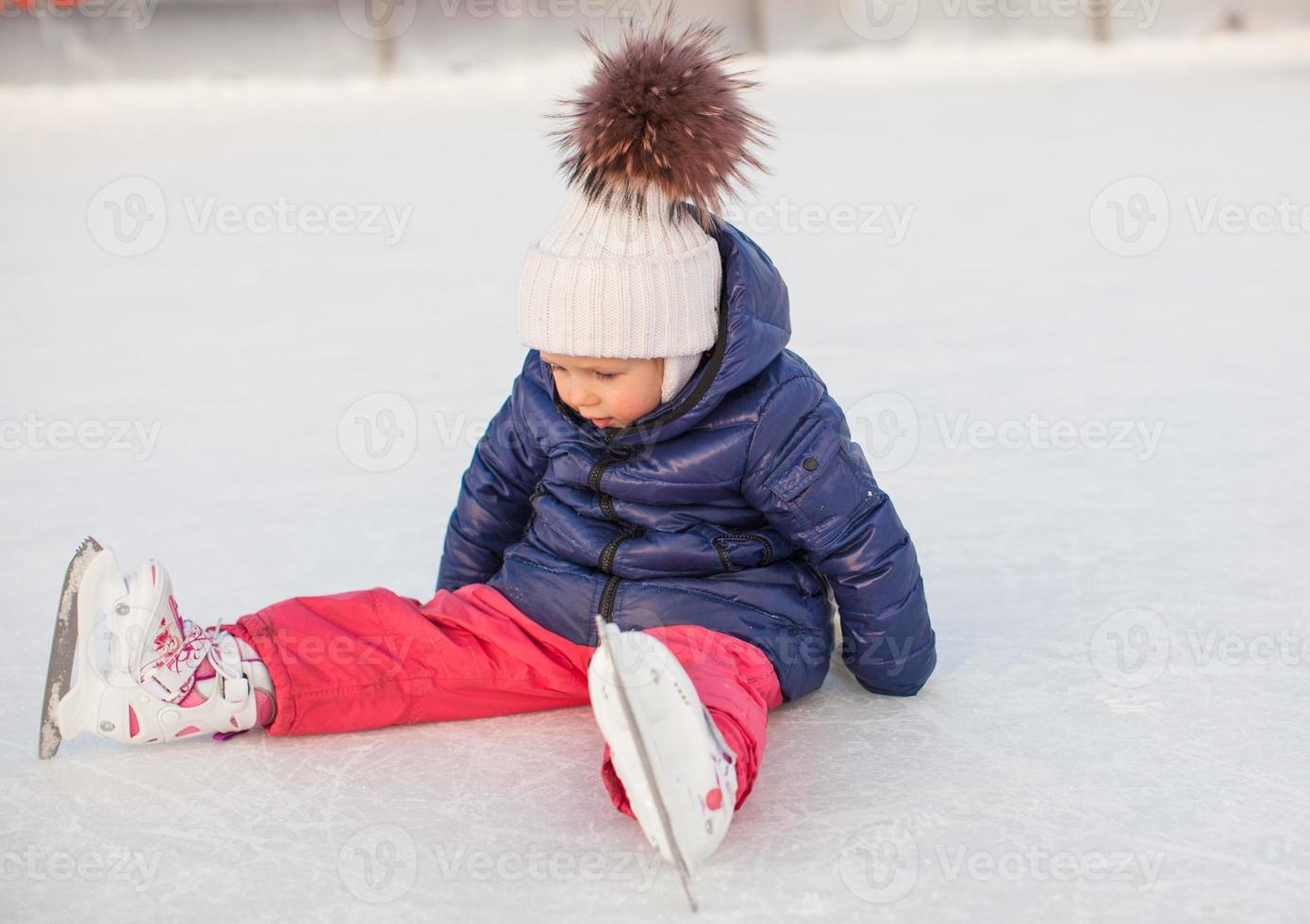 liten förtjusande flicka Sammanträde på is med skridskor efter de falla foto