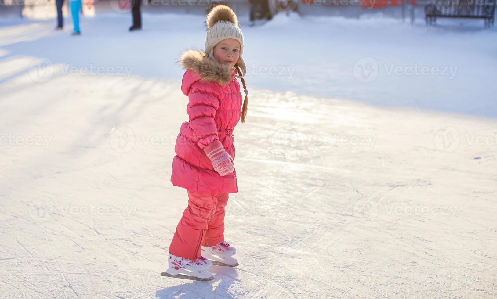 förtjusande liten flicka njuter skridskoåkning på de isbana foto