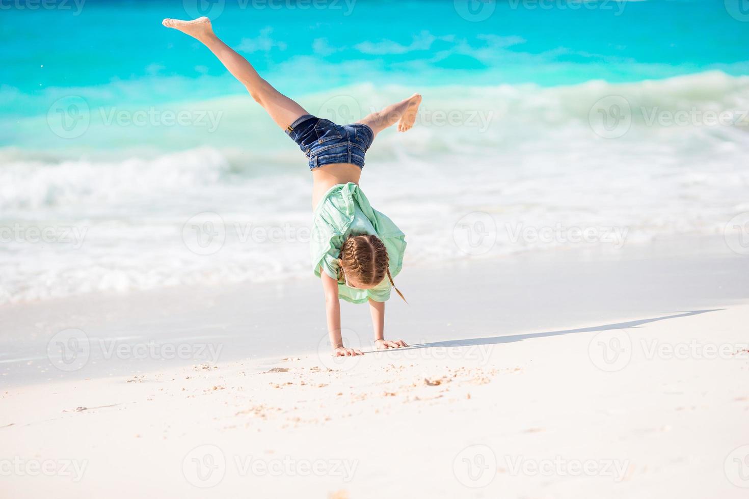 förtjusande liten flicka på strand har en massa av roligt. sportig aktiva unge framställning de hjul foto