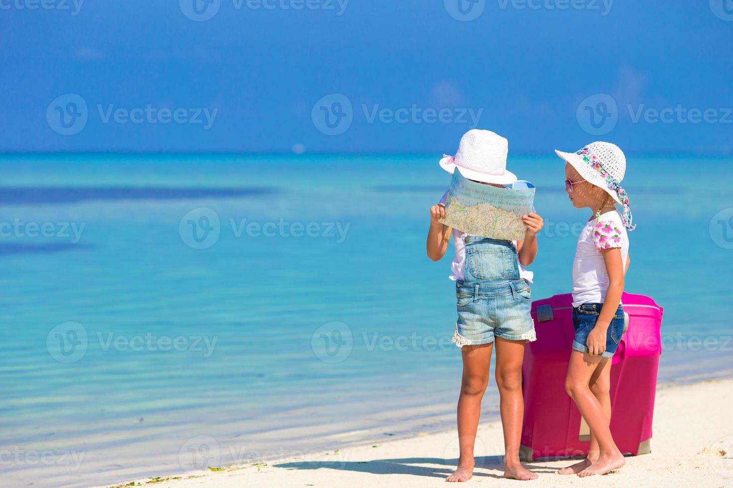 liten flickor med stor resväska och Karta på tropisk strand foto