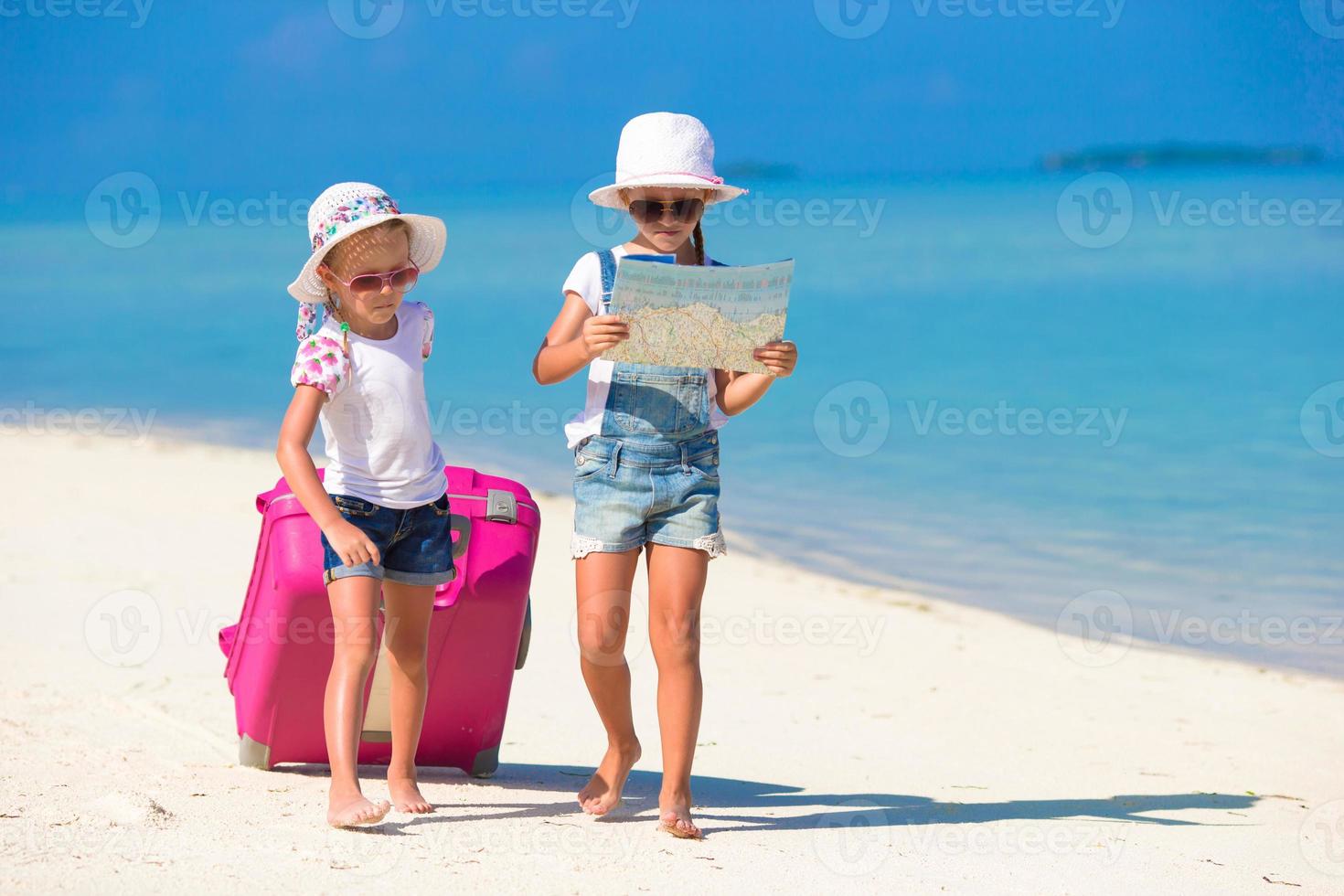 liten flickor med stor resväska och Karta på tropisk strand foto