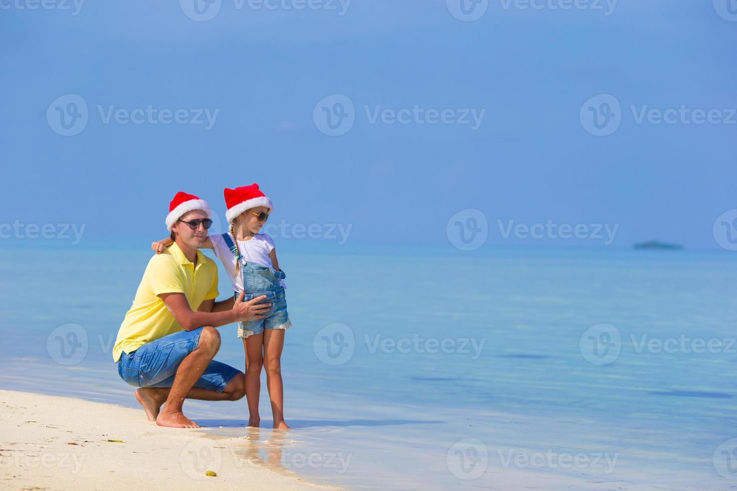 liten flicka och Lycklig pappa i santa hatt under strand semester foto