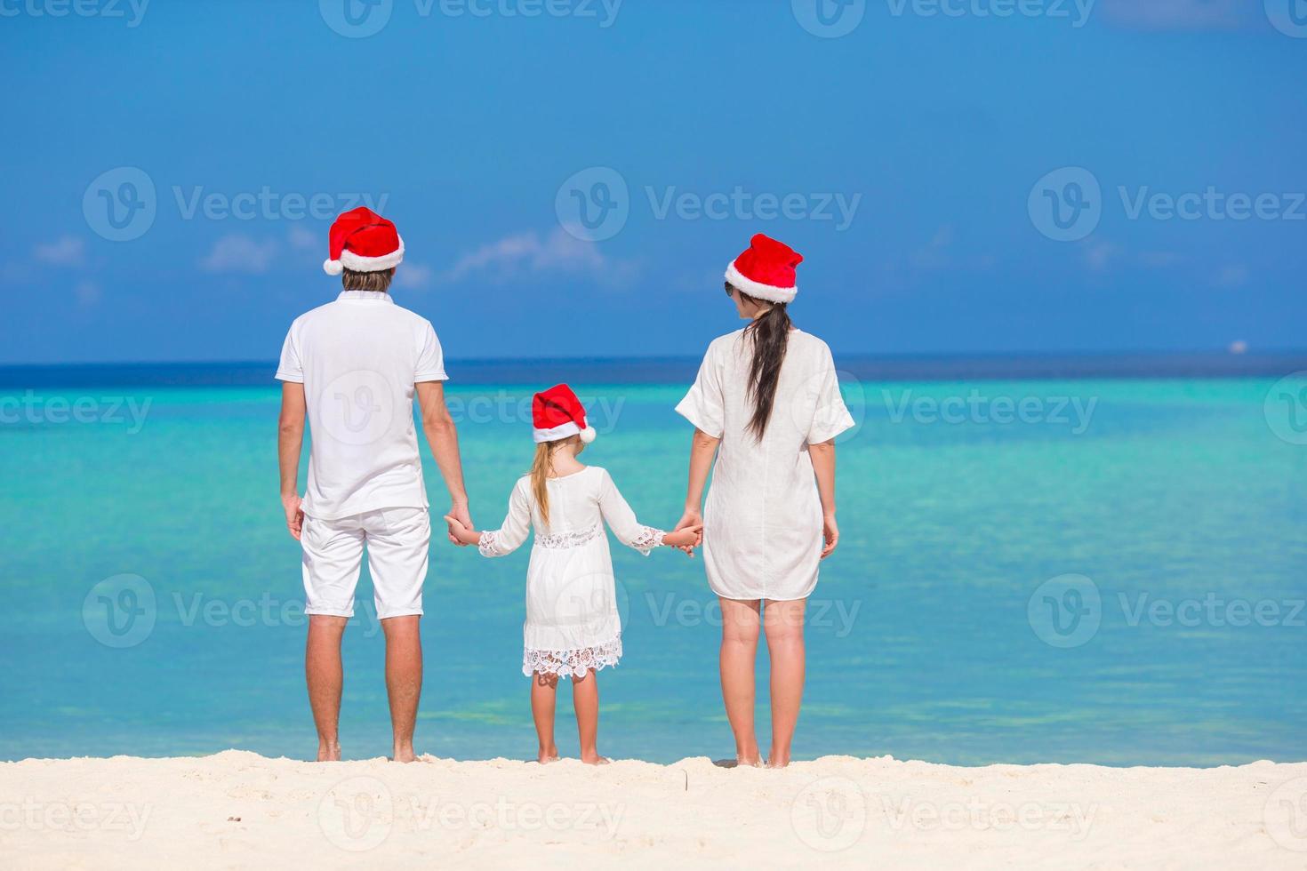 Lycklig familj av tre i santa hattar under tropisk semester foto