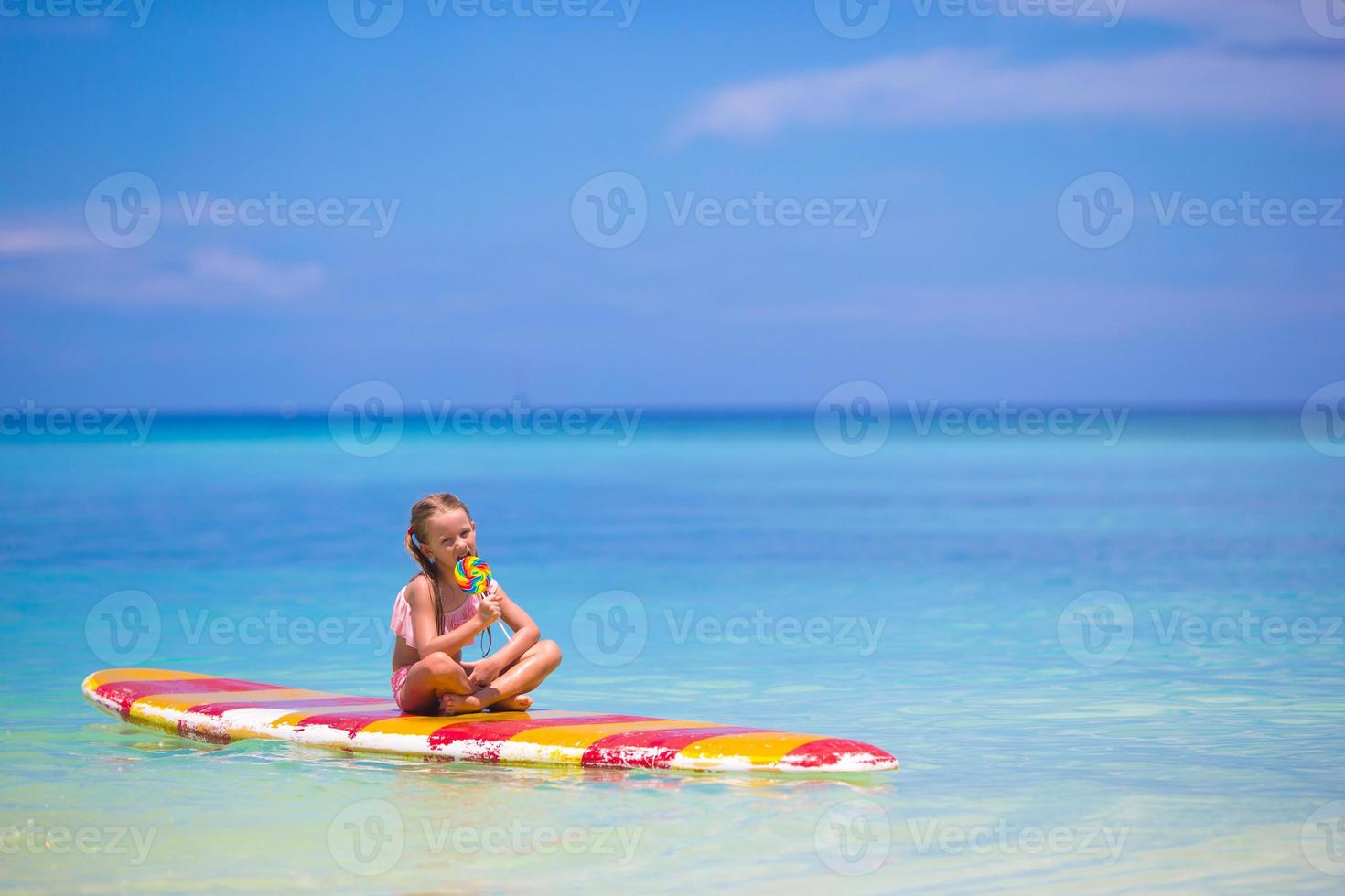 liten flicka med klubba ha roligt på surfingbräda i de hav foto