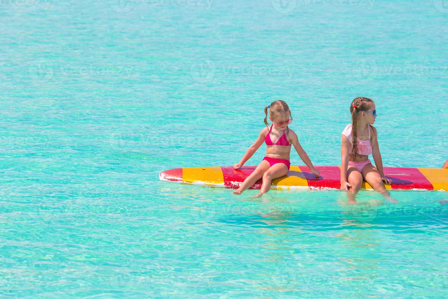 liten förtjusande flickor på en surfingbräda i de turkos hav foto