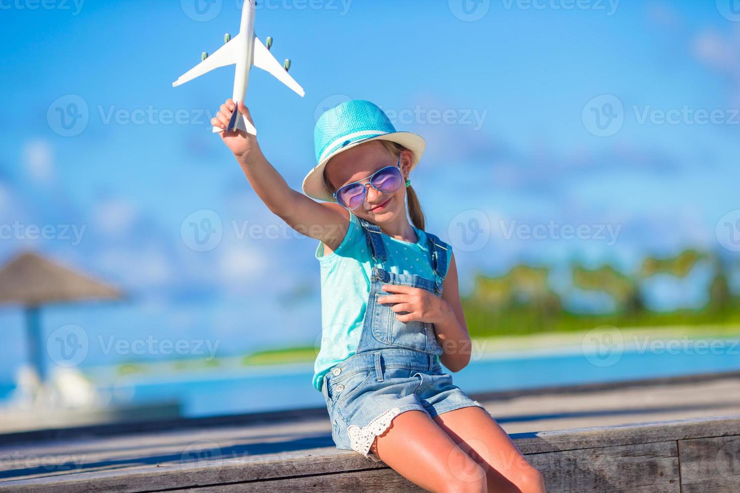 glad liten flicka med leksaksflygplan i händerna på den vita sandstranden foto