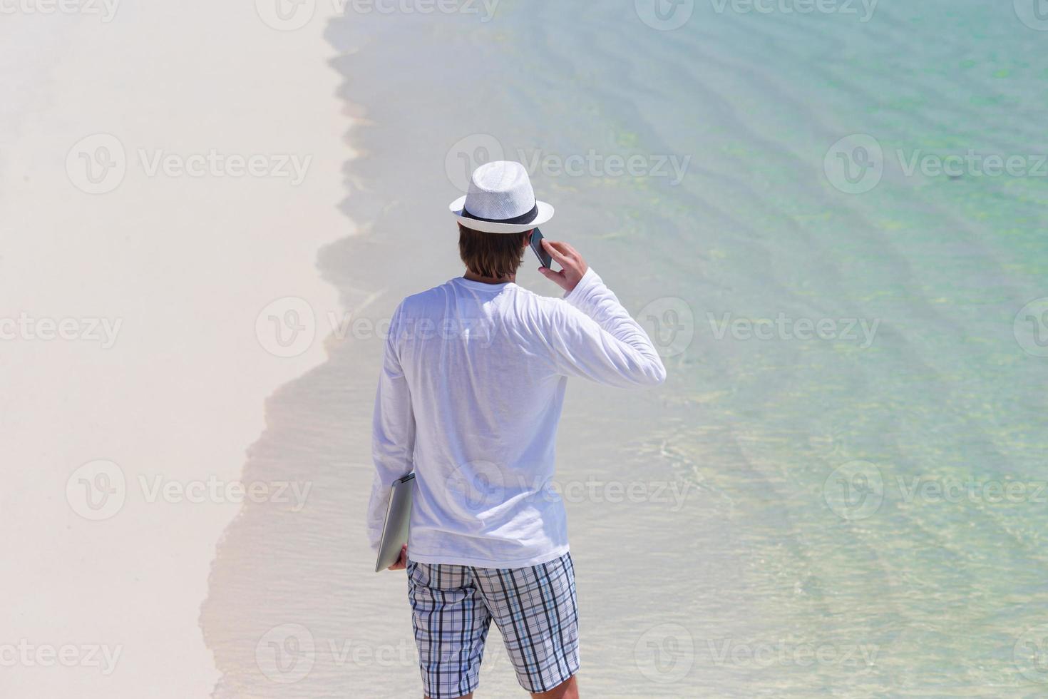 ung man talande förbi cell telefon på tropisk strand foto