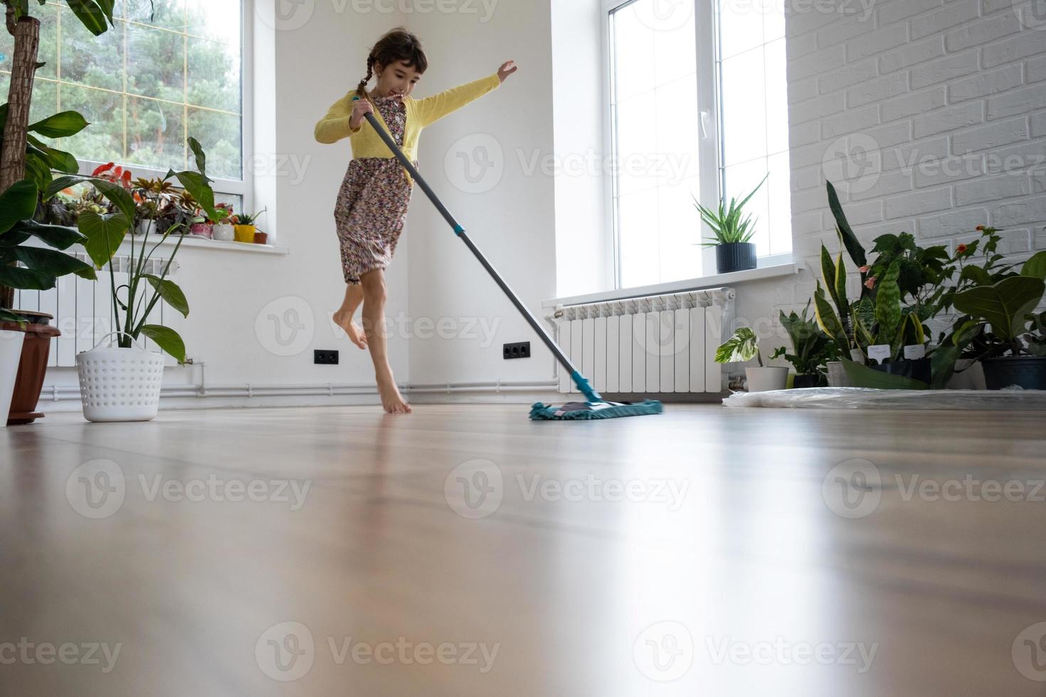 en flicka danser med en mopp till rena de golv i en ny hus - allmän rengöring i ett tömma rum, de glädje av rör på sig, hjälp med de hushållsarbete foto