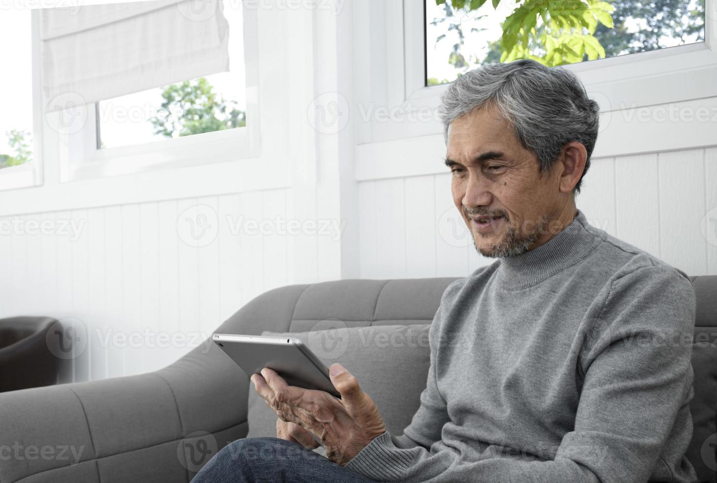 porträtt äldre senior asiatisk man sitter nära glas fönster i de morgon- till arbete från Hem och kontroll hans företag på hans bärbar dator på tabell allvarligt, mjuk och selektiv fokus. foto