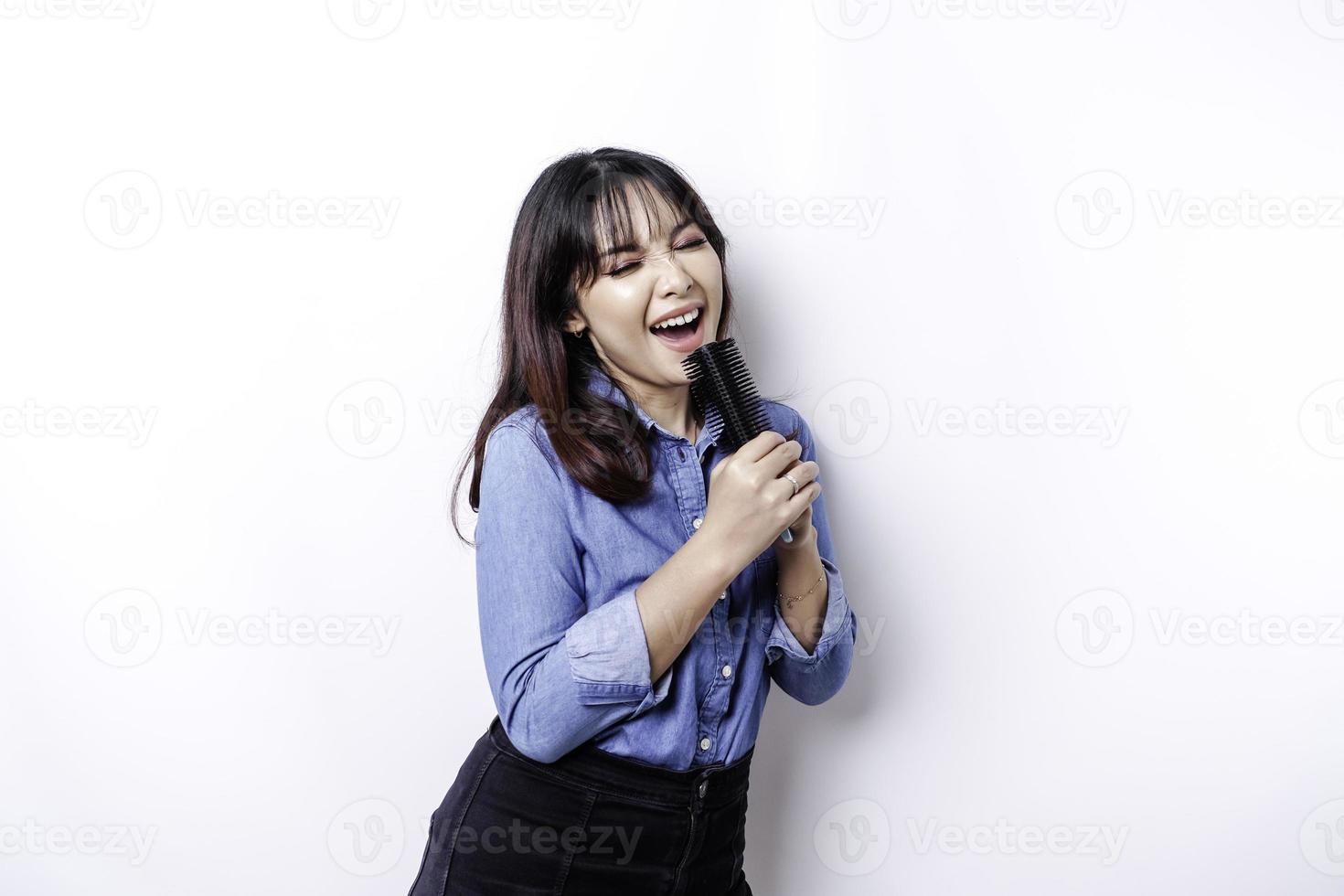 porträtt av sorglös asiatisk kvinna, har roligt karaoke, sång i mikrofon medan stående över vit bakgrund foto
