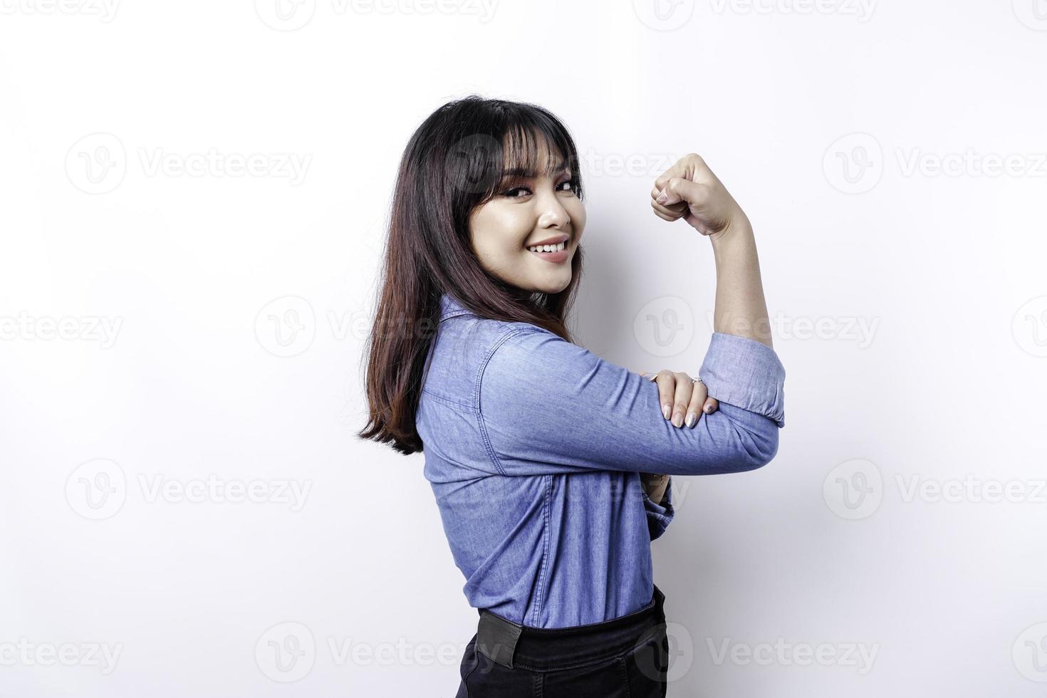 upphetsad asiatisk kvinna bär en blå skjorta som visar stark gest förbi lyft henne vapen och muskler leende stolt foto
