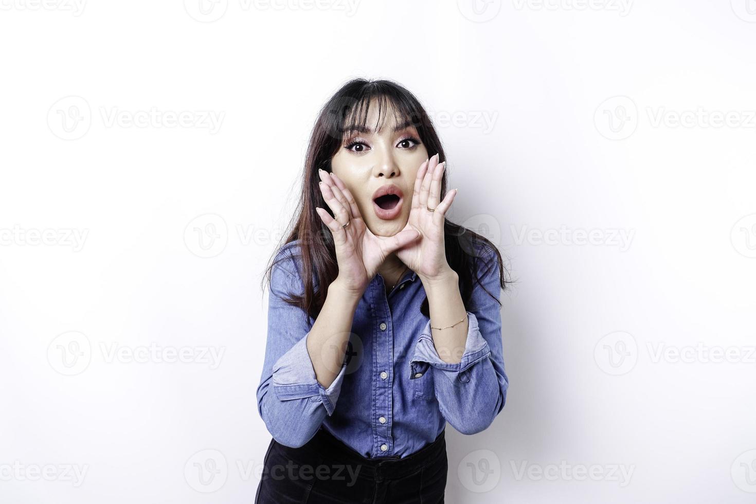 ung skön kvinna bär en blå skjorta skrikande och skrikande högt med en hand på henne mun. kommunikation begrepp. foto