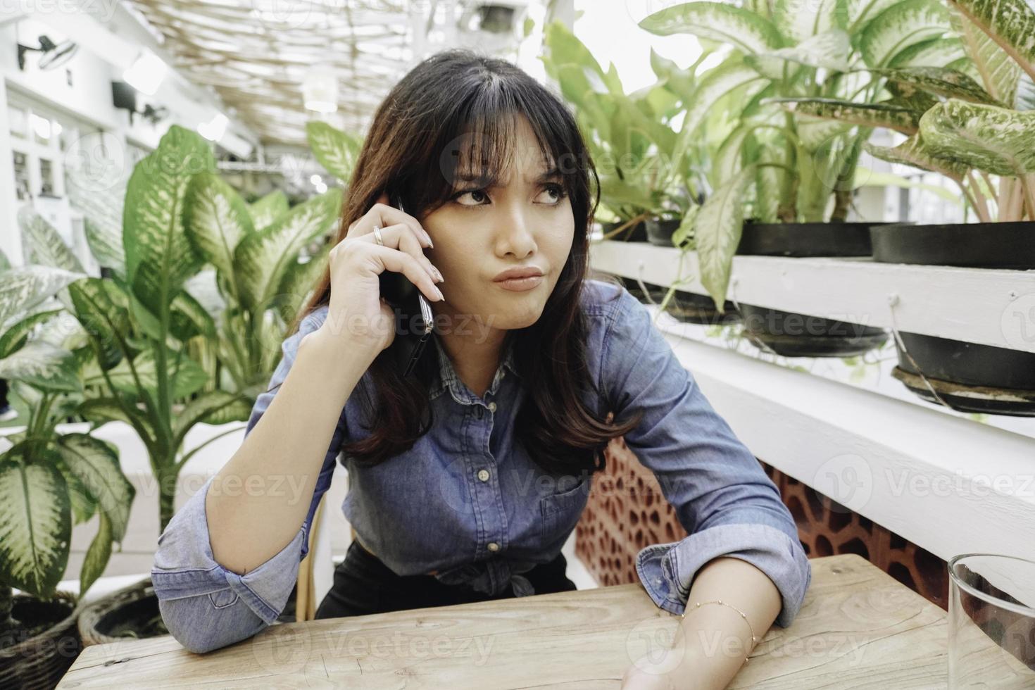 en missnöjd ung asiatisk kvinna utseende missnöjd bär blå skjorta irriterad ansikte uttryck innehav henne telefon foto