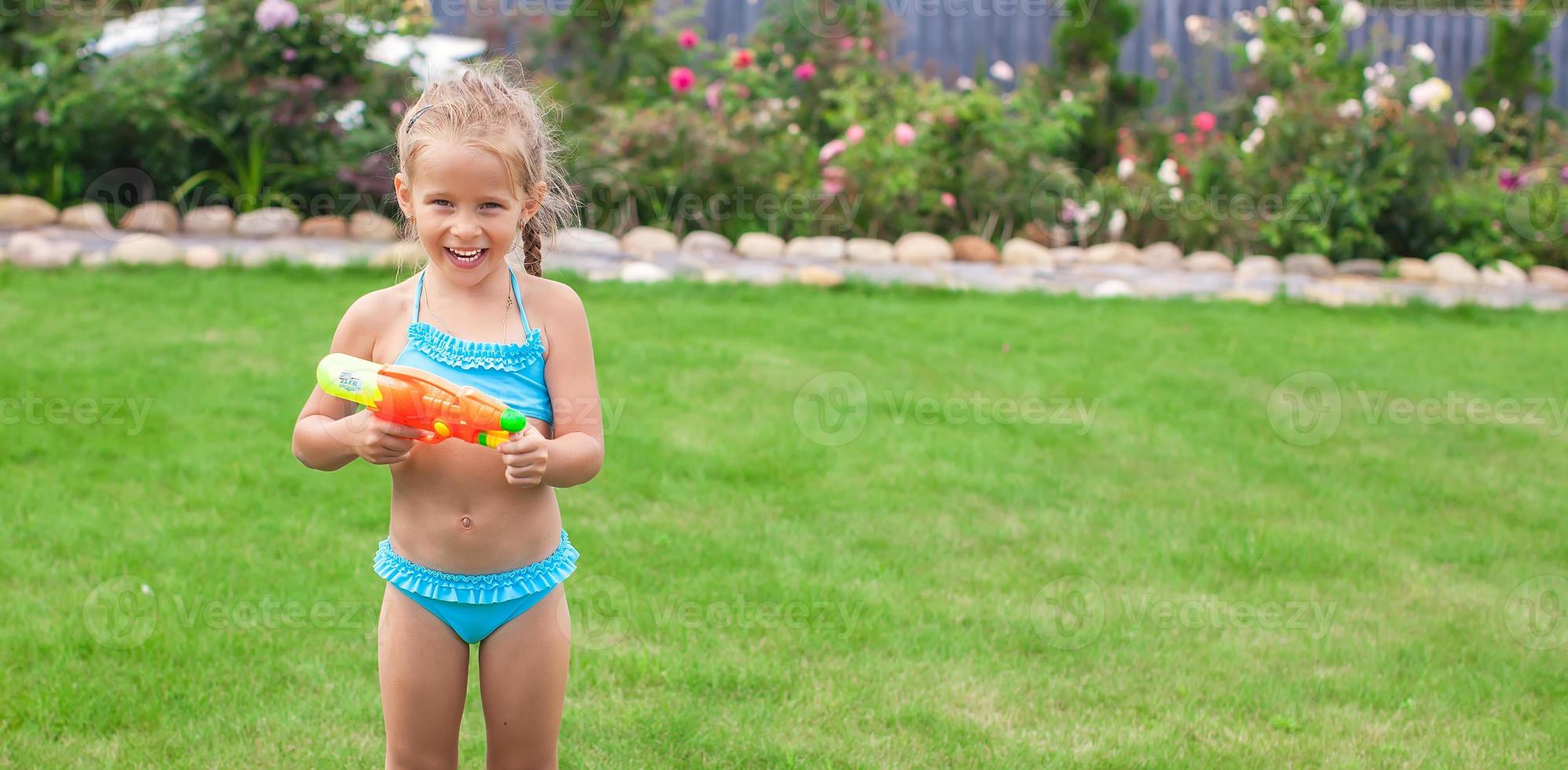 liten Lycklig flicka spelar med vatten pistol utomhus- i solig sommar dag foto