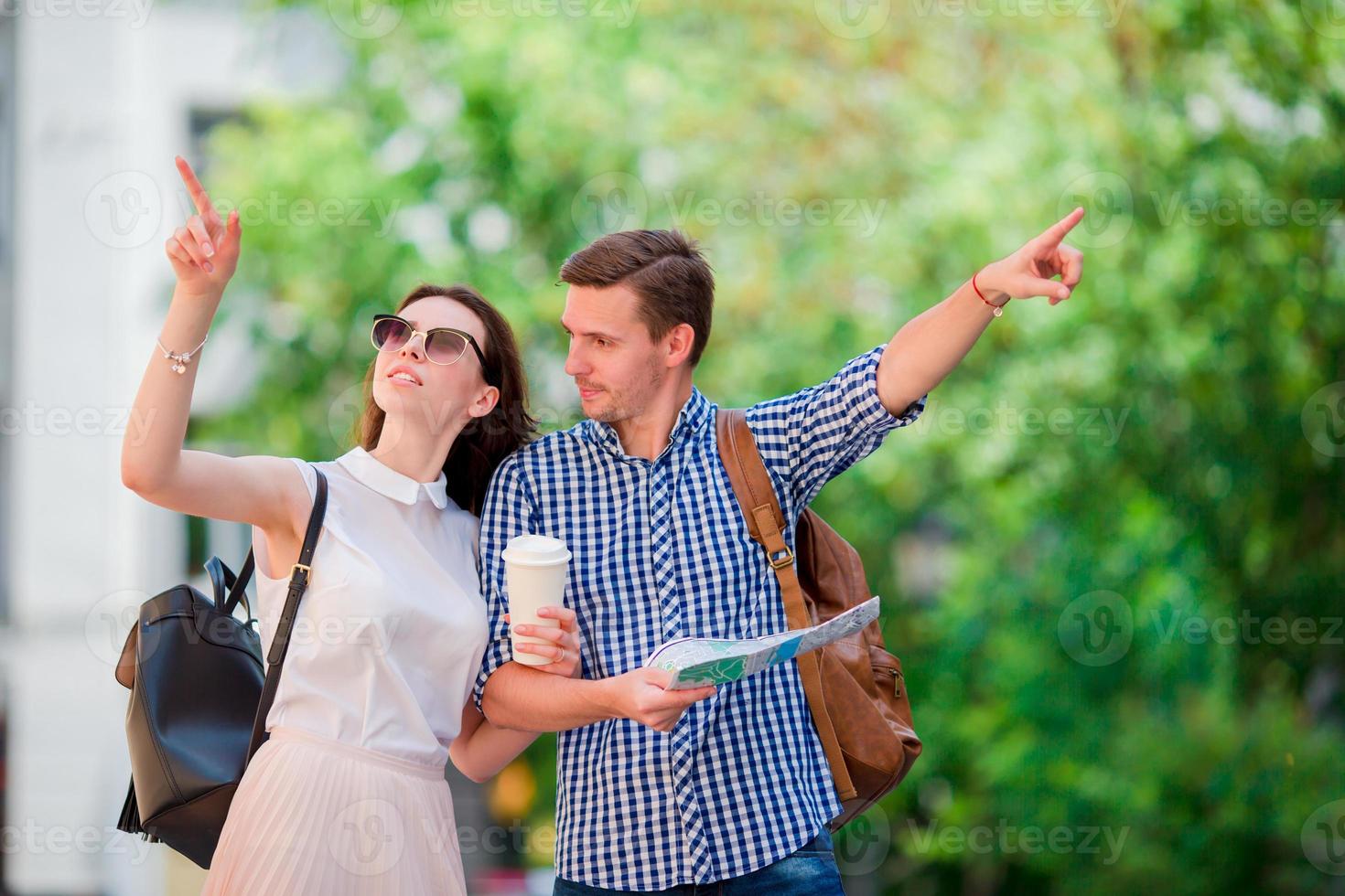 Lycklig turist par reser i Europa leende Lycklig. caucasian vänner med stad Karta i Sök av attraktioner. ung man med varm kaffe och skön kvinna med stor Karta foto
