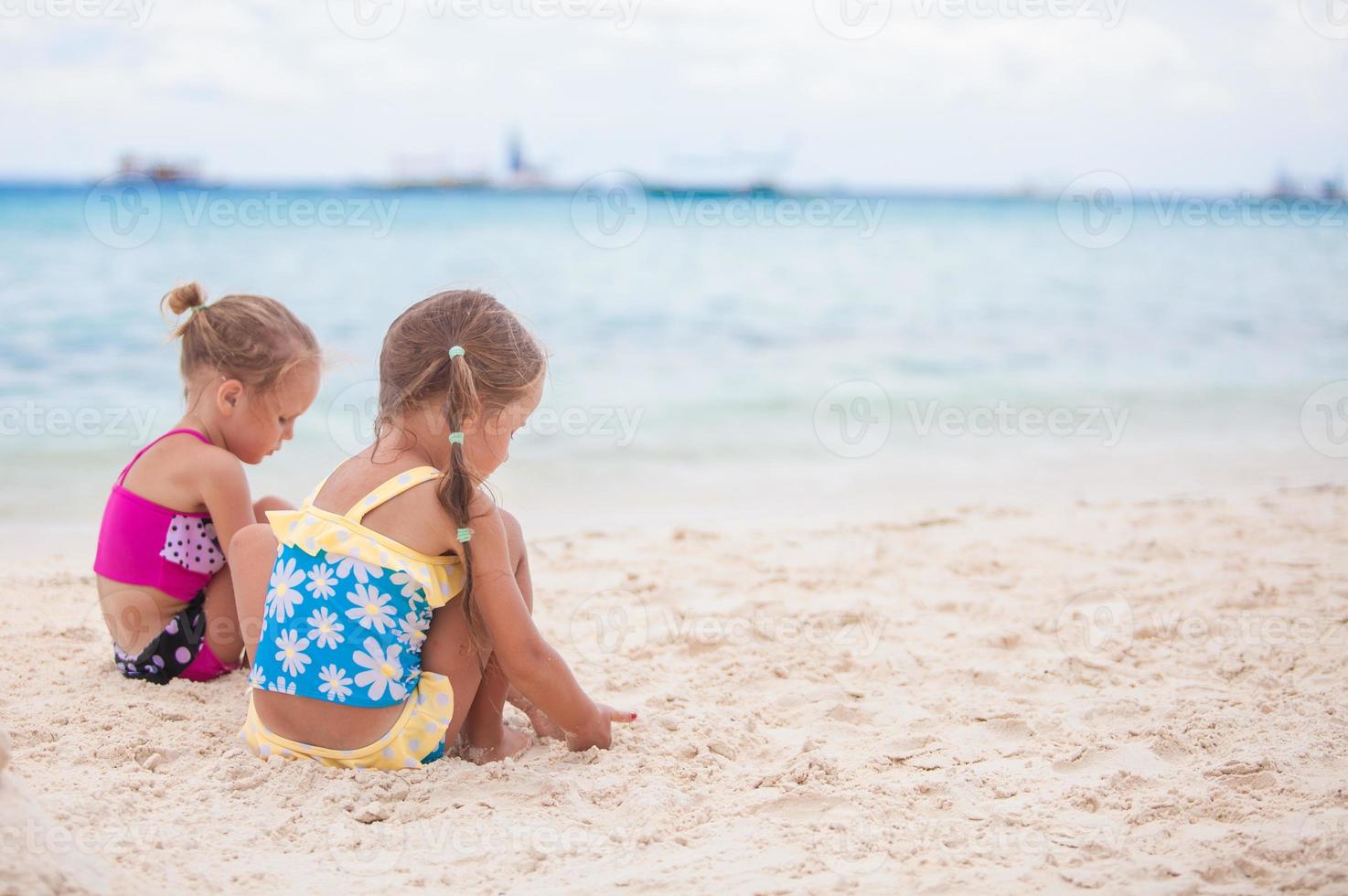 två liten systrar i trevlig baddräkter spelar på sandig strand foto