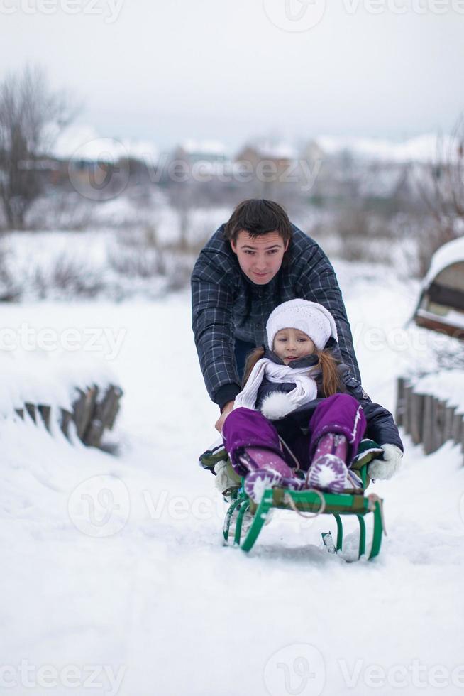 ung far med hans bebis dotter i en släde rida och njut av solig vinter- dag foto