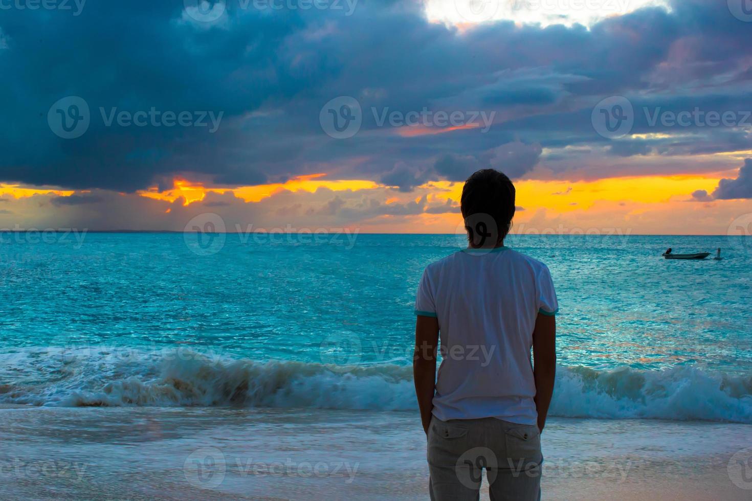 ung man njuter solnedgång under strand semester foto