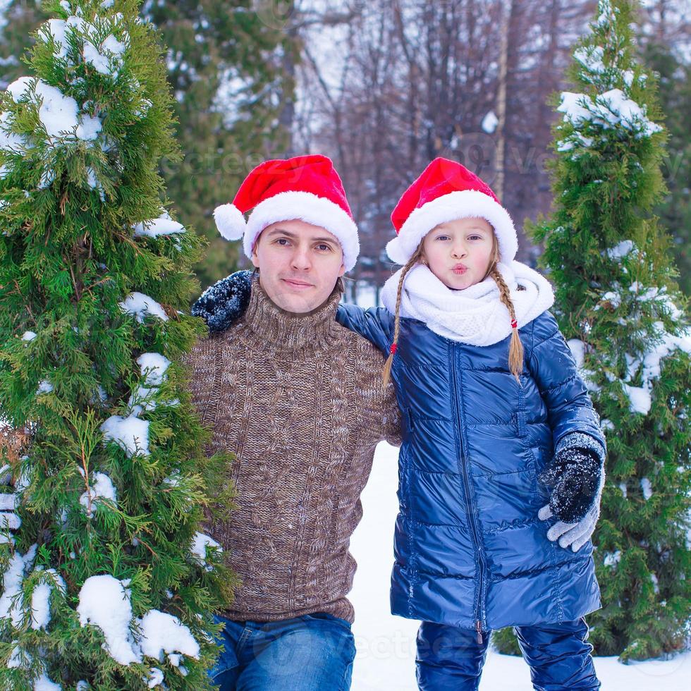 Lycklig far och unge i santa hattar med jul träd utomhus- foto