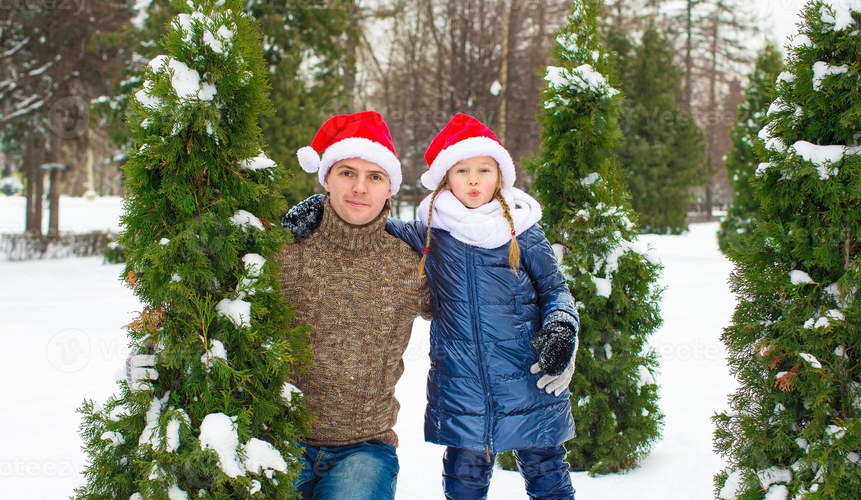 Lycklig far och liten flicka i santa hattar med jul träd utomhus- foto